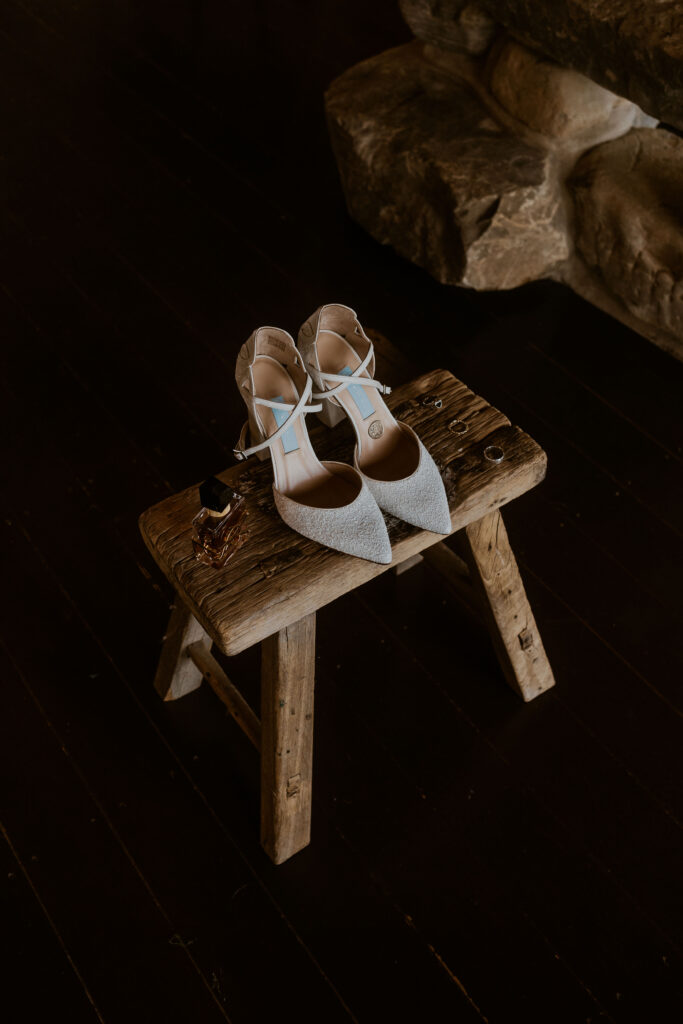 Alternative brides wedding shoes by Charlotte Mills captured on a wooden stool at Willow Marsh Farm captured by a relaxed wedding photographer