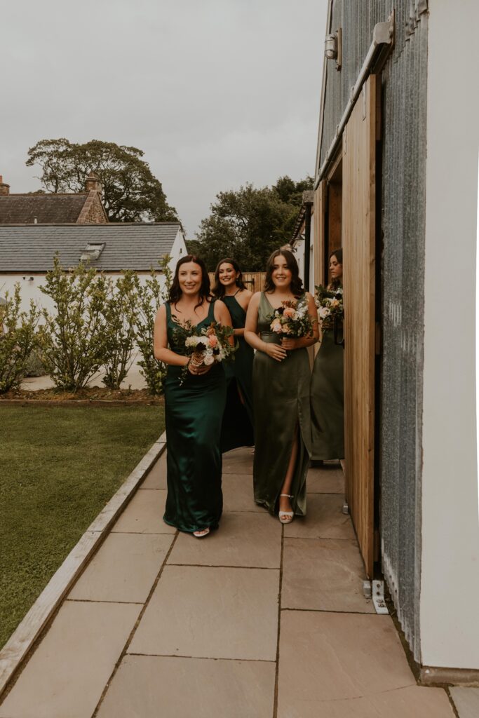 bridesmaids in beautiful green silk dresses walking to the ceremony at Eden Barn wedding venue