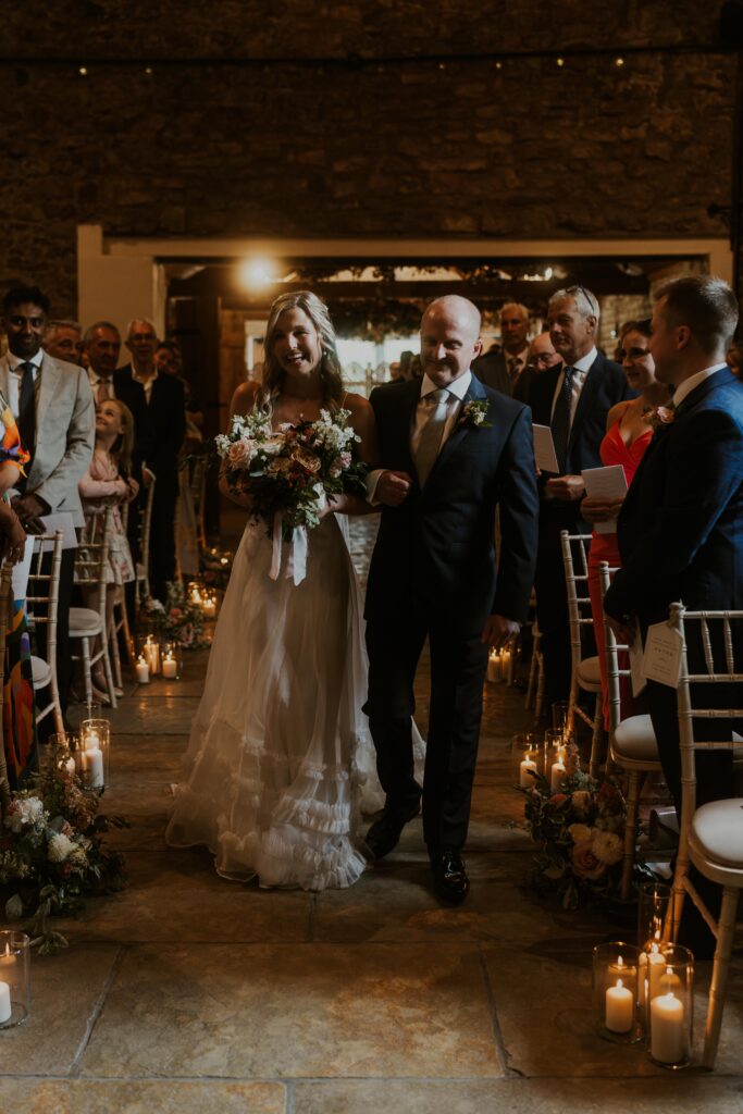 The bride and her Dad in beautiful half penny london wedding dress walking down the isle at eden barn wedding venue
