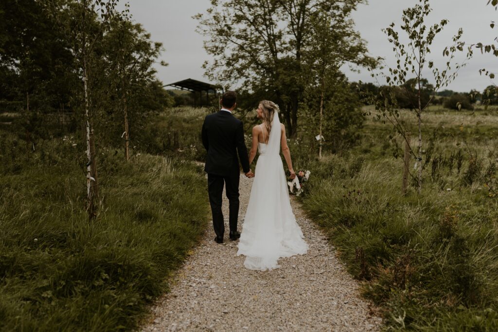 Newly married couple, adventurous and wild at heart, embarking on their next great adventure together, hand in hand at eden barn wedding venue