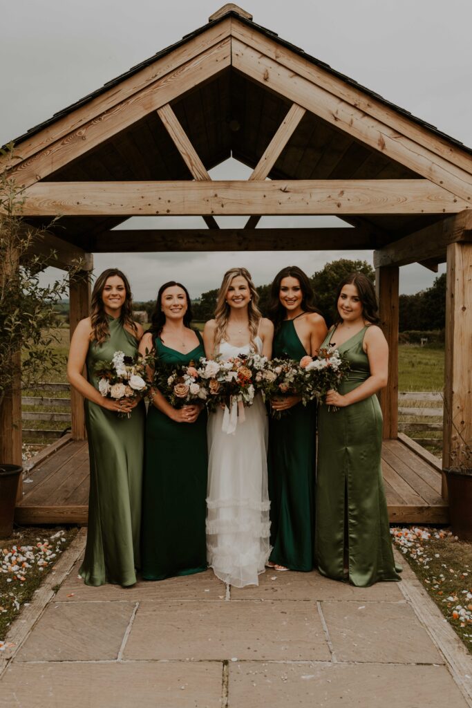 relaxed wedding photographer capturing group shots of the bride enjoying her time with her bridesmaids in green silk dresses, smiling and having fun