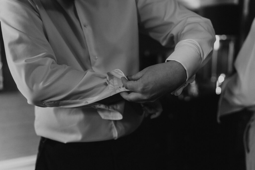 Groom buttoning his shirt up in black and white