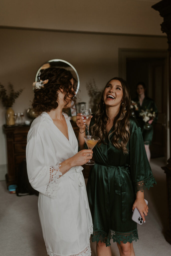 bride and bridesmaid laughing together before the wedding ceremony with their green matching robes
