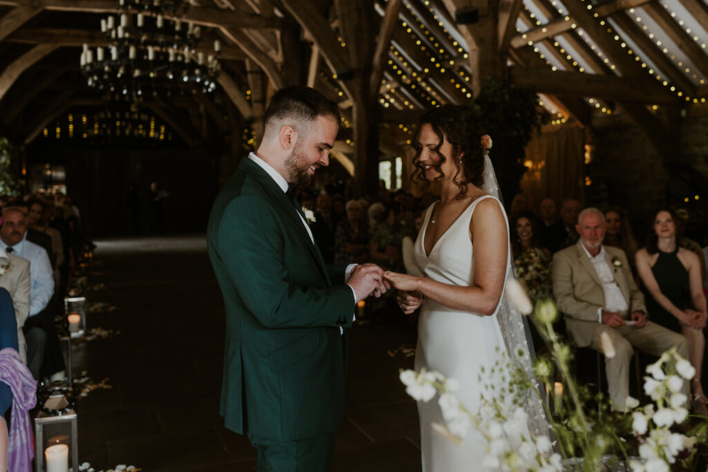 Bride and Groom exchanging rings in their ceremony at tithe barn wedding venue 