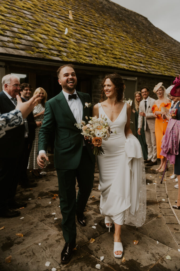 the bride and groom smiling and laughing as they walk down their confetti line at tithe barn wedding venue