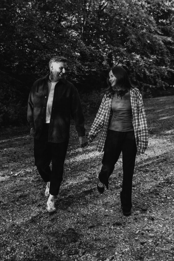 relaxed wedding photographer husband and wife team capturing couple laughing and walking hand in hand in the woods in black and white