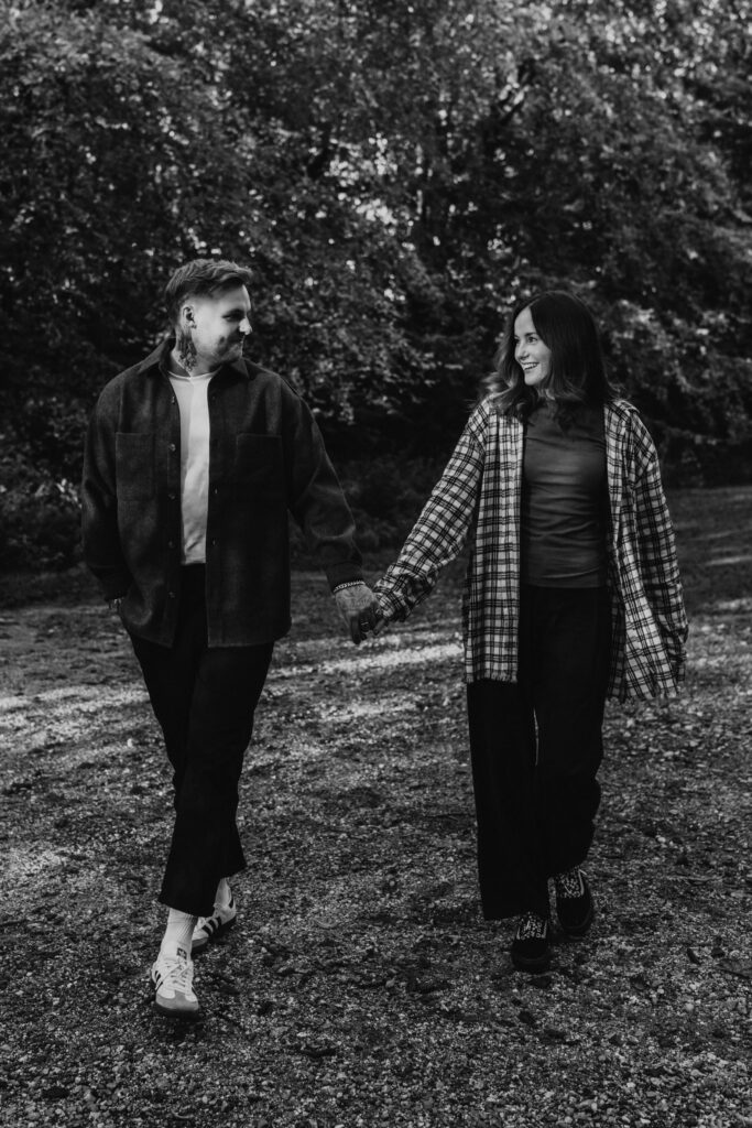 relaxed wedding photographer husband and wife team capturing alternative couple laughing and walking hand in hand in the woods in black and white 
