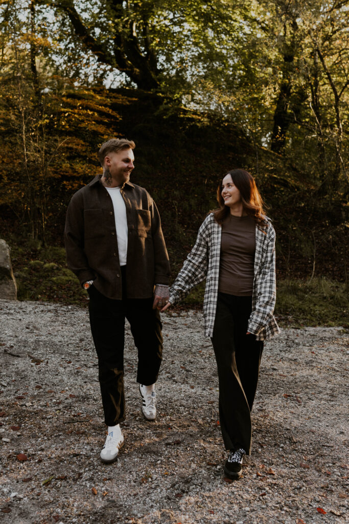 relaxed wedding photographer husband and wife team capturing alternative couple laughing and walking hand in hand in the woods on their sunset pre wedding shoot