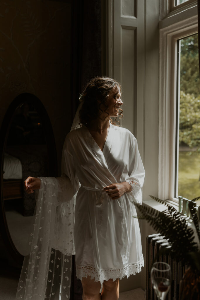 bride looking out the window on her wedding morning in her white robe

