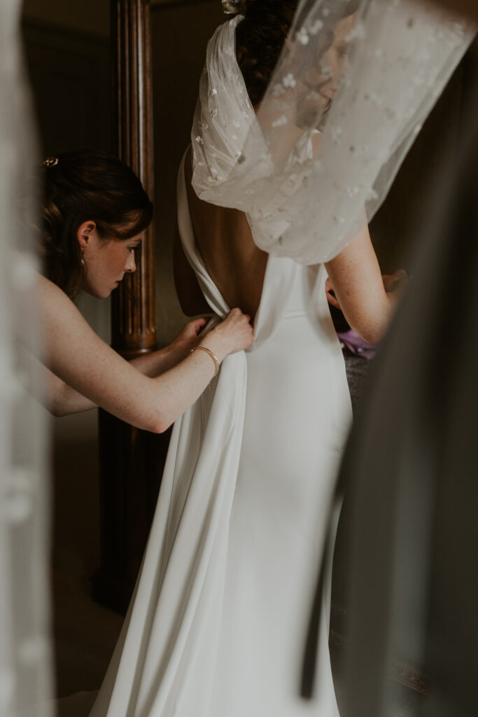 the bride getting into her white wedding gown ahead of her ceremony at tithe barn wedding venue
